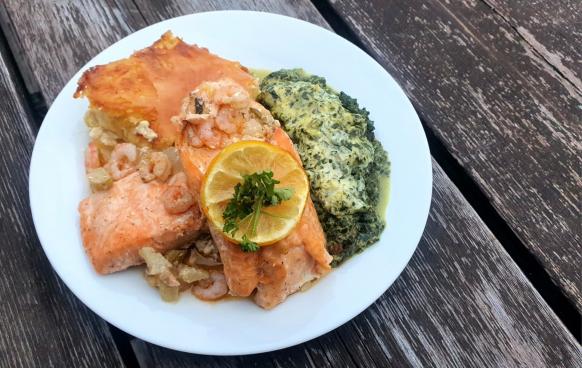 Teller mit Lachs, Krabben, Kartoffelgratin und Spinat, garniert mit einer Zitronenscheibe