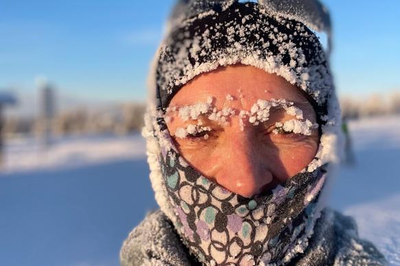 Frau mit Buff und Mütze bekleidet und Eis an Kleidung und Haaren