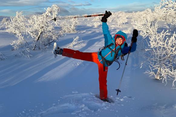 Frau steht auf einem Bein im Tiefschnee und trägt Schneeschuhe
