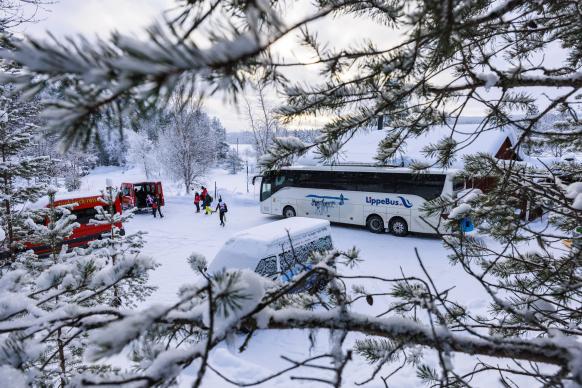 Blick durch Zweige auf Reisebus von Lippe Bus und Autos von Rucksack Reisen auf dem Parkplatz des Wintercamps Idre