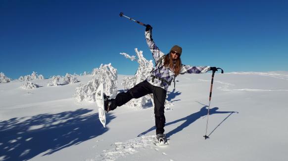 Frau steht in Winterlandschaft mit Schneeschuhen auf einem Bein