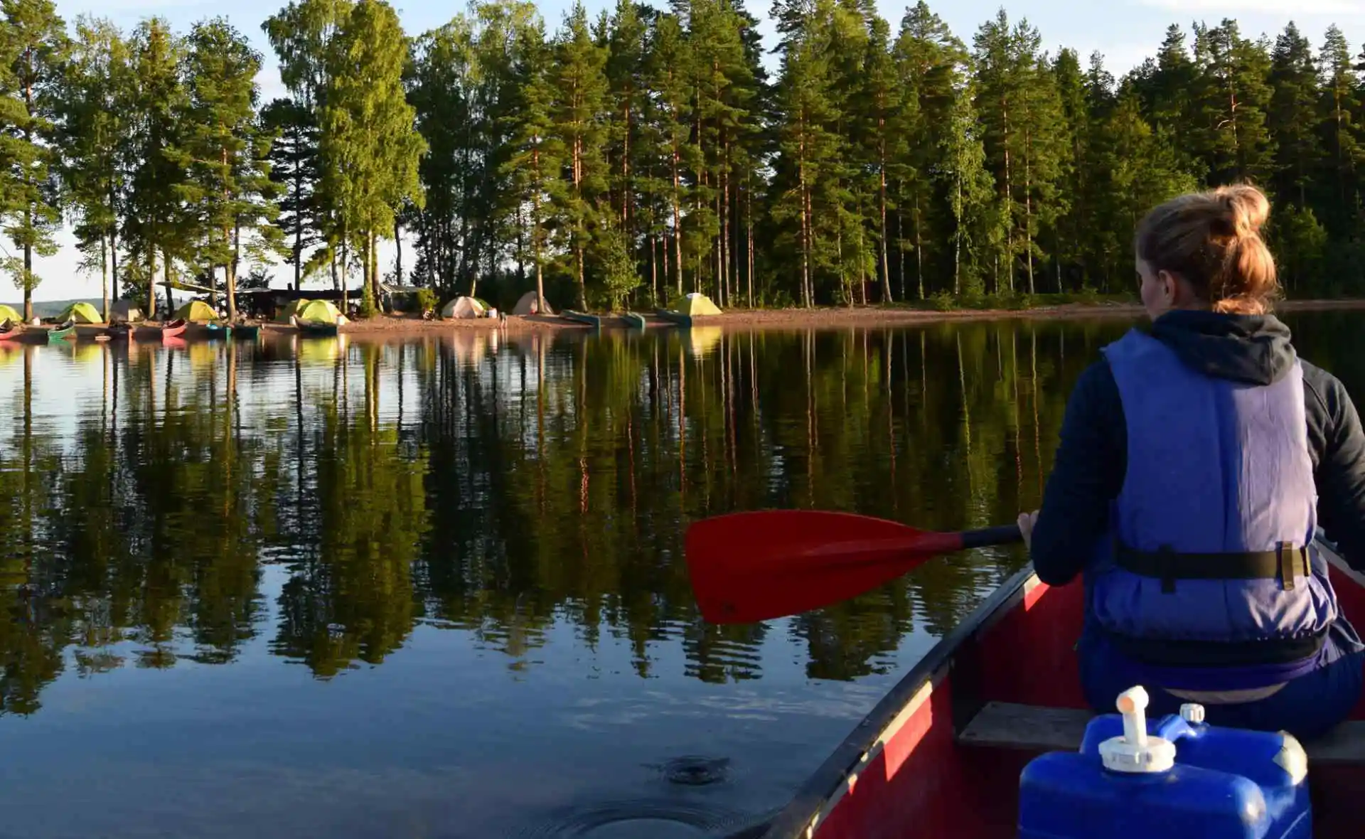 Frau im Kanu auf spiegelglattem See mit Zelten am Ufer
