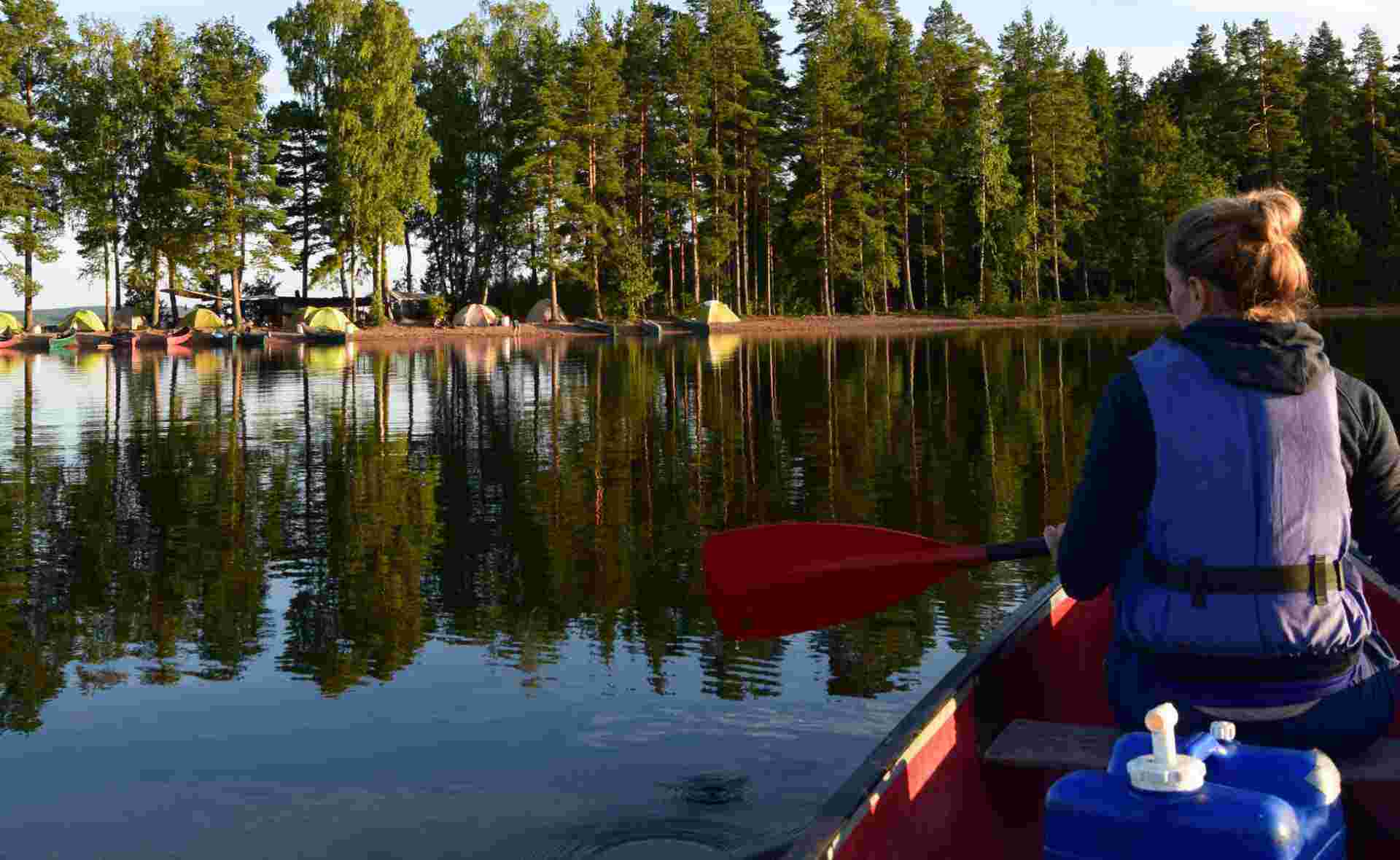 Frau im Kanu auf spiegelglattem See mit Zelten am Ufer